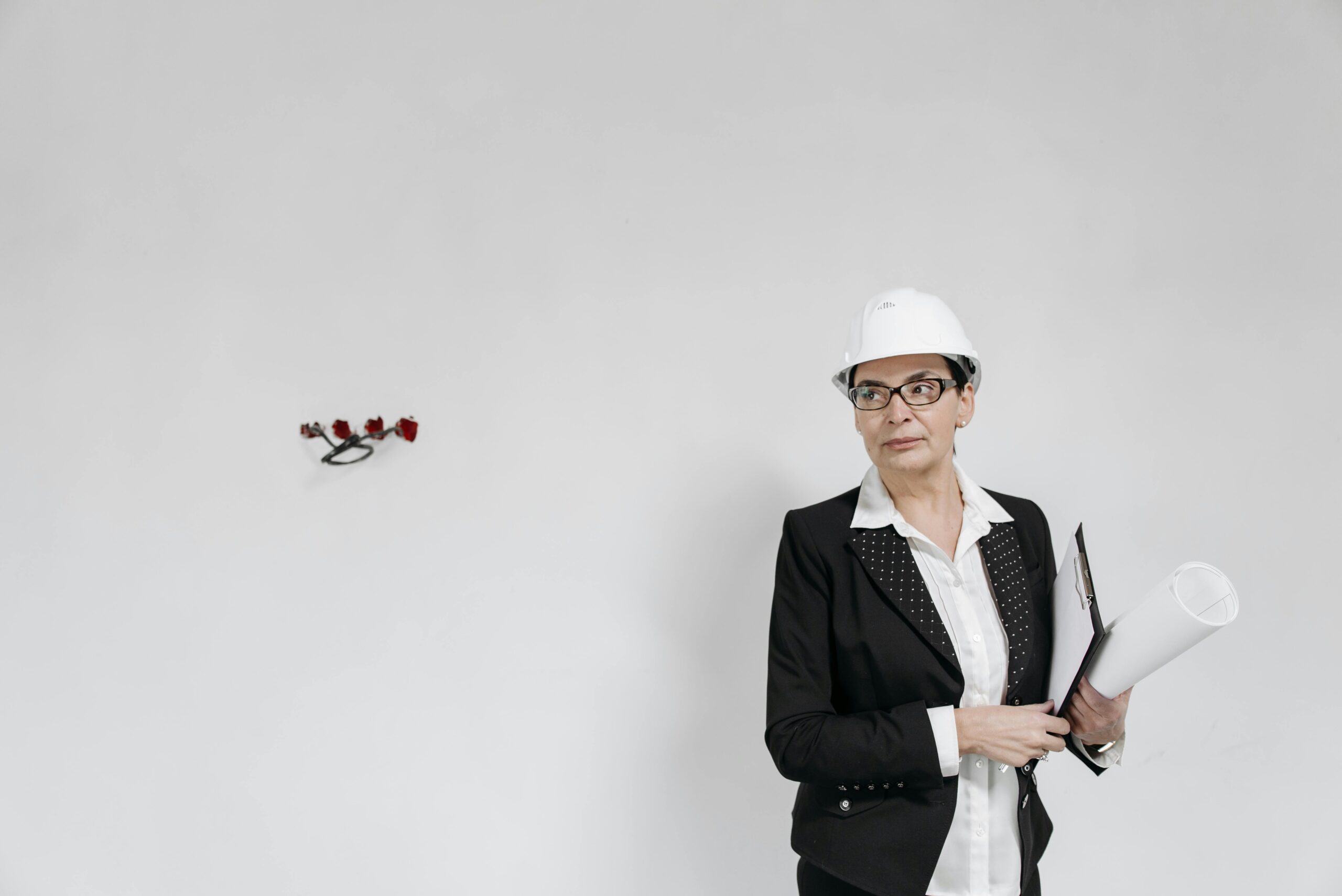 Businesswoman in formal attire with a hard hat holding blueprints against a white background.