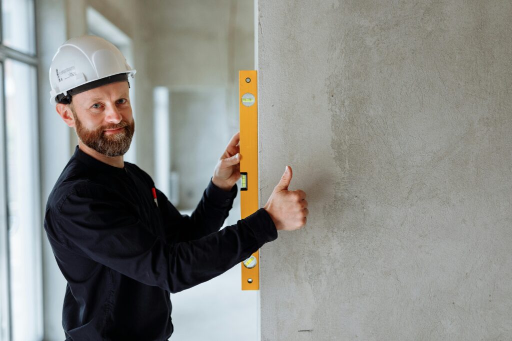 Confident male construction worker using a spirit level on a concrete wall for precise alignment indoors.
